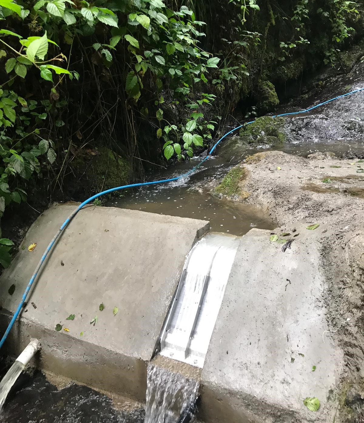 The same forest stream after the intake was built: a compact concrete structure with an ADENCO Coanda screen and the supply pipe leaving it
