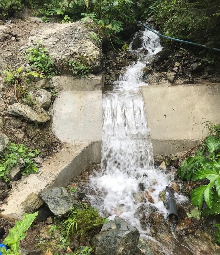 The same creek after the retrofit, water flowing in a thin sheet over an ADENCO Coanda screen built into a new concrete weir